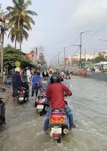 أشخاص يركبون الدراجات البخارية على طول طريق مليء بالمياه في بنغالورو، ولاية كارناتاكا ، الهند. (رويترز)